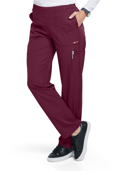 Woman wearing FLAT FRONT STRAIGHT LEG PANT C52106 medical scrubs with multiple pockets and black sneakers, standing in a profile pose showcasing the garment.