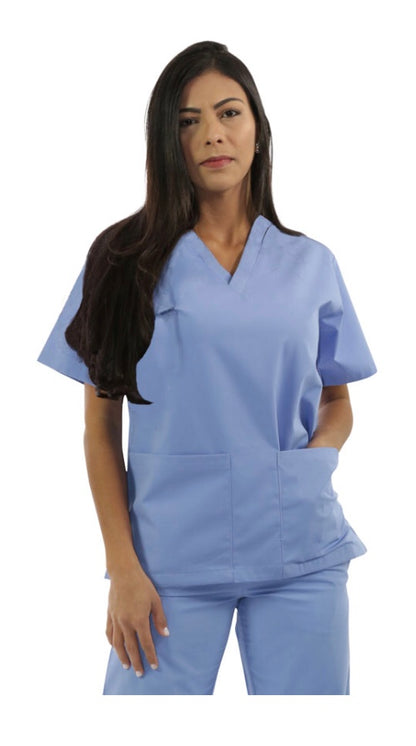 A woman in blue scrubs stands with her hands in her pockets against a white background.