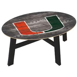 An oval coffee table with a distressed wood top featuring abstract, partially painted red and green sections, supported by black angular legs.