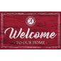 A wooden sign featuring the text "welcome to our home" with an alabama crimson tide logo on red painted background.