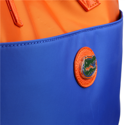 Close-up of a bright orange and blue bag with a round The Phyllis Handbag (University of Florida Gators) logo badge attached to it.