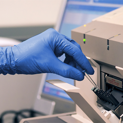A person wearing a pair of AMMEX Professional Cerulean Nitrile PF Exam Gloves inserts a usb drive into a slot on a laboratory machine.