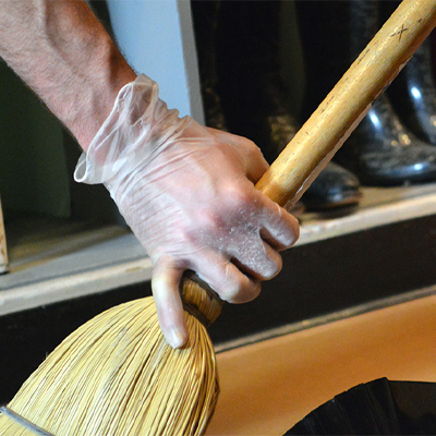Close-up of a hand wearing X3 Stretch Hybrid Poly Disposable Gloves gripping a wooden broom handle, with visible dust particles on the glove.