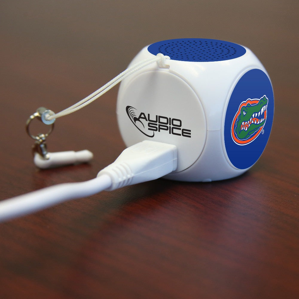 Portable speaker from Florida Gators MX-100 Cubio Mini Bluetooth® Speaker Plus Selfie Remote on a wooden desk, connected to a white cable.