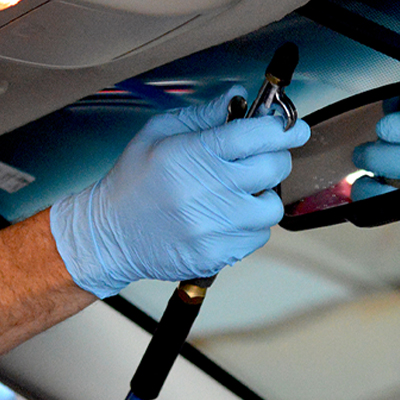 Close-up of hands wearing X3 Blue Nitrile Industrial Latex Free Disposable Gloves (Case of 1000), repairing a car's windshield with a tool.