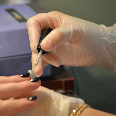 A person wearing X3 Stretch Hybrid Poly Disposable Gloves fills a syringe from a vial, focusing intently on the task, with a blue box in the background.