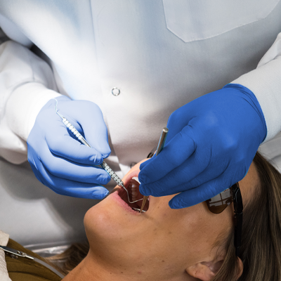 A dentist in AMMEX Exam Blue Nitrile PF Disposable Gloves performing a dental procedure on a female patient.