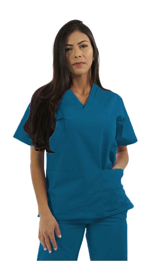A woman in blue medical scrubs stands with her hands in her pockets, looking slightly to her left.