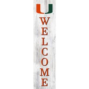 Vertical "welcome" sign with a serif font, featuring a green and orange letter "u" at the top, set against a white wooden plank background.