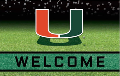 Miami Hurricanes Crumb Rubber Door Mat featuring a green and orange "u" above a "welcome" sign, set against a backdrop of a grass field with a blurred stadium in the distance.