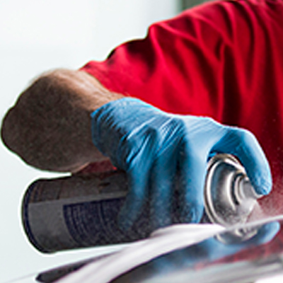 A worker in X3 Blue Nitrile Industrial Latex Free Disposable Gloves using a power tool to polish or grind a metal surface, focusing intently on the task.