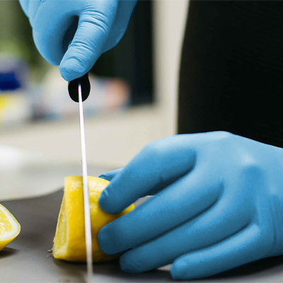 A person in X3 Blue Nitrile Industrial Latex Free Disposable Gloves (Case of 1000) conducting an experiment by dipping a litmus strip into a lemon slice to test its acidity.