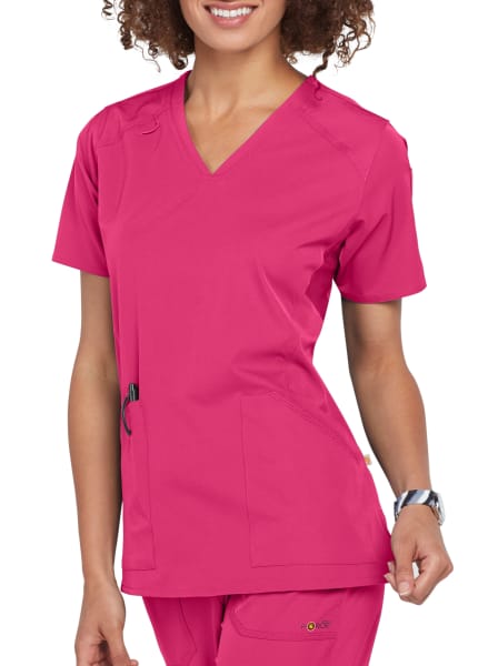 A woman in a bright pink MULTI-POCKET V-NECK TOP C12106 uniform smiling, focusing on her upper body.