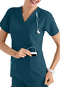 Nurse in CROSS FLEX V-NECK MEDIA SCRUB TOP C12110 using smartphone with stethoscope around neck, smiling and looking to her side.