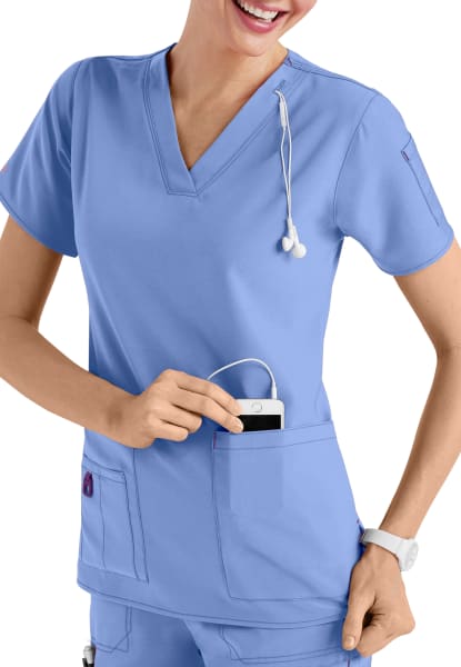 A smiling healthcare professional in CROSS FLEX V-NECK MEDIA SCRUB TOP C12110 placing a mobile device into her pocket.