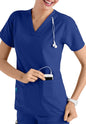 A smiling healthcare worker in a CROSS FLEX V-NECK MEDIA SCRUB TOP C12110 with a stethoscope around her neck, inserting a smartphone into her pocket.