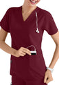 A smiling healthcare worker in a CROSS FLEX V-NECK MEDIA SCRUB TOP C12110 uniform using a mobile device with headphones attached.