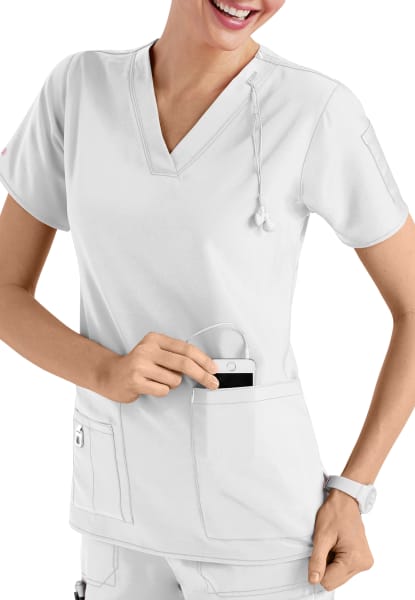 A smiling healthcare worker in a white uniform inserts a CROSS FLEX V-NECK MEDIA SCRUB TOP C12110 into her pocket.