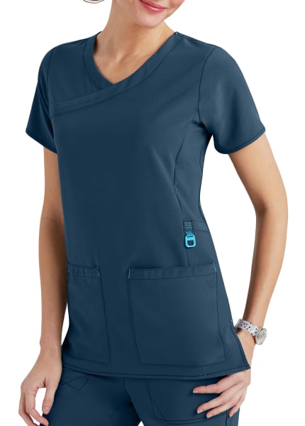 A woman in a navy blue medical scrub top featuring a v-neck, short sleeves, and two large front pockets, standing with one hand on her hip.