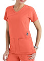 Woman in coral scrubs with a v-neck top featuring lower front pockets, standing with one hand on her hip.
