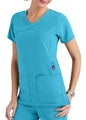 A woman in teal scrubs with a v-neck top featuring large pockets, standing against a plain background.