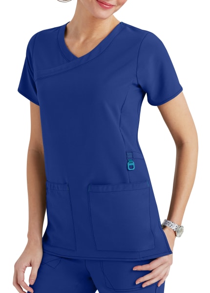 Woman wearing a blue scrub top with v-neck and two front pockets, accentuated with a teal id tag holder.