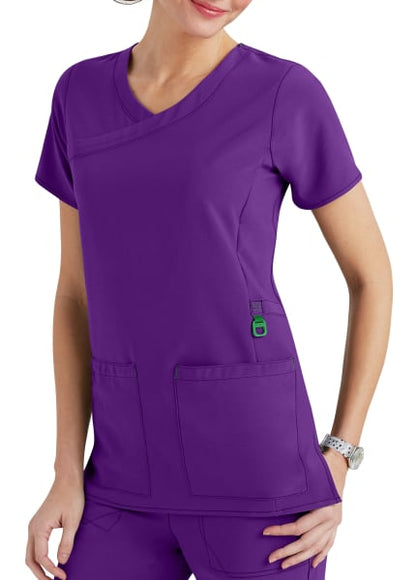 Woman in purple medical scrubs with a v-neck, short sleeves, and multiple pockets, standing with one hand lightly resting on her hip.
