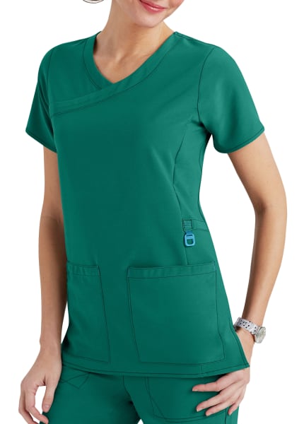A woman wearing a green scrub suit with a v-neck and multiple pockets, standing against a white background.