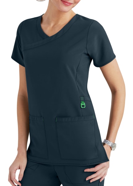 A woman wearing a dark gray medical scrub top with multiple pockets, featuring a stylish v-neck and green accents.