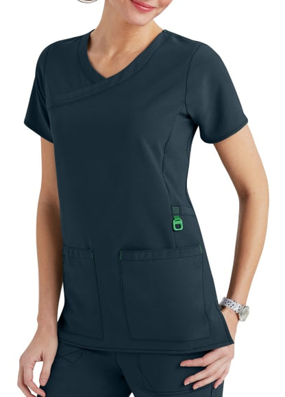 A woman wearing a dark gray medical scrub top with multiple pockets, featuring a stylish v-neck and green accents.