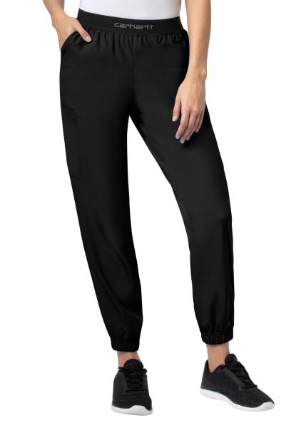 A woman wearing black Carhartt Liberty Comfort Cargo Jogger Scrub Pants (Women's C54106) and black sneakers, with her left hand resting on her thigh.