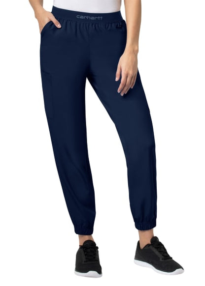 A woman stands wearing Carhartt Liberty Comfort Cargo Jogger Scrub Pants in dark blue and black sneakers, midsection close-up, on a white background.